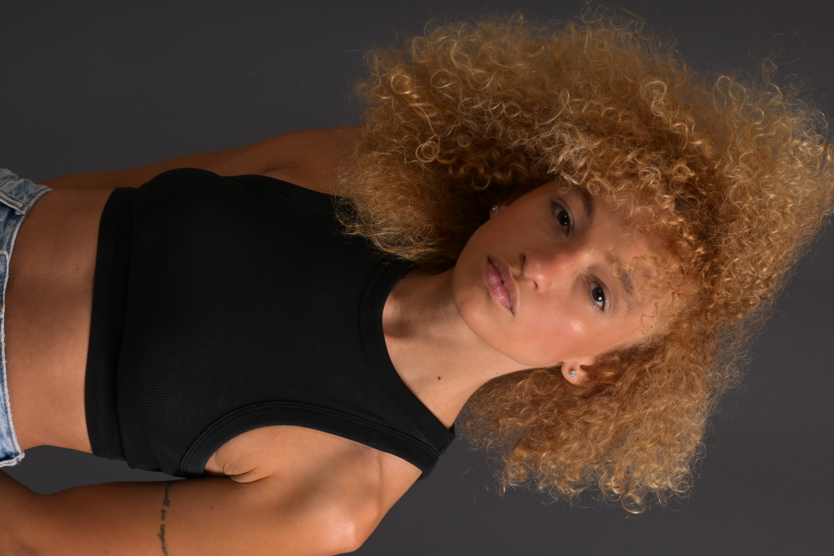 Three-quarter portrait of Nalu in a black top and jeans against a dark background.
