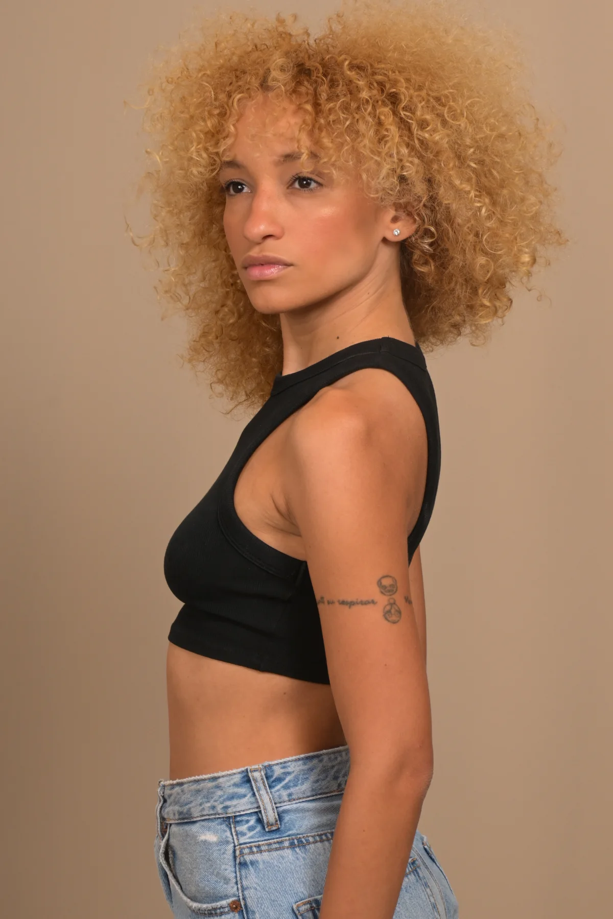 Side view of Nalu in a black top and jeans against a plain background.