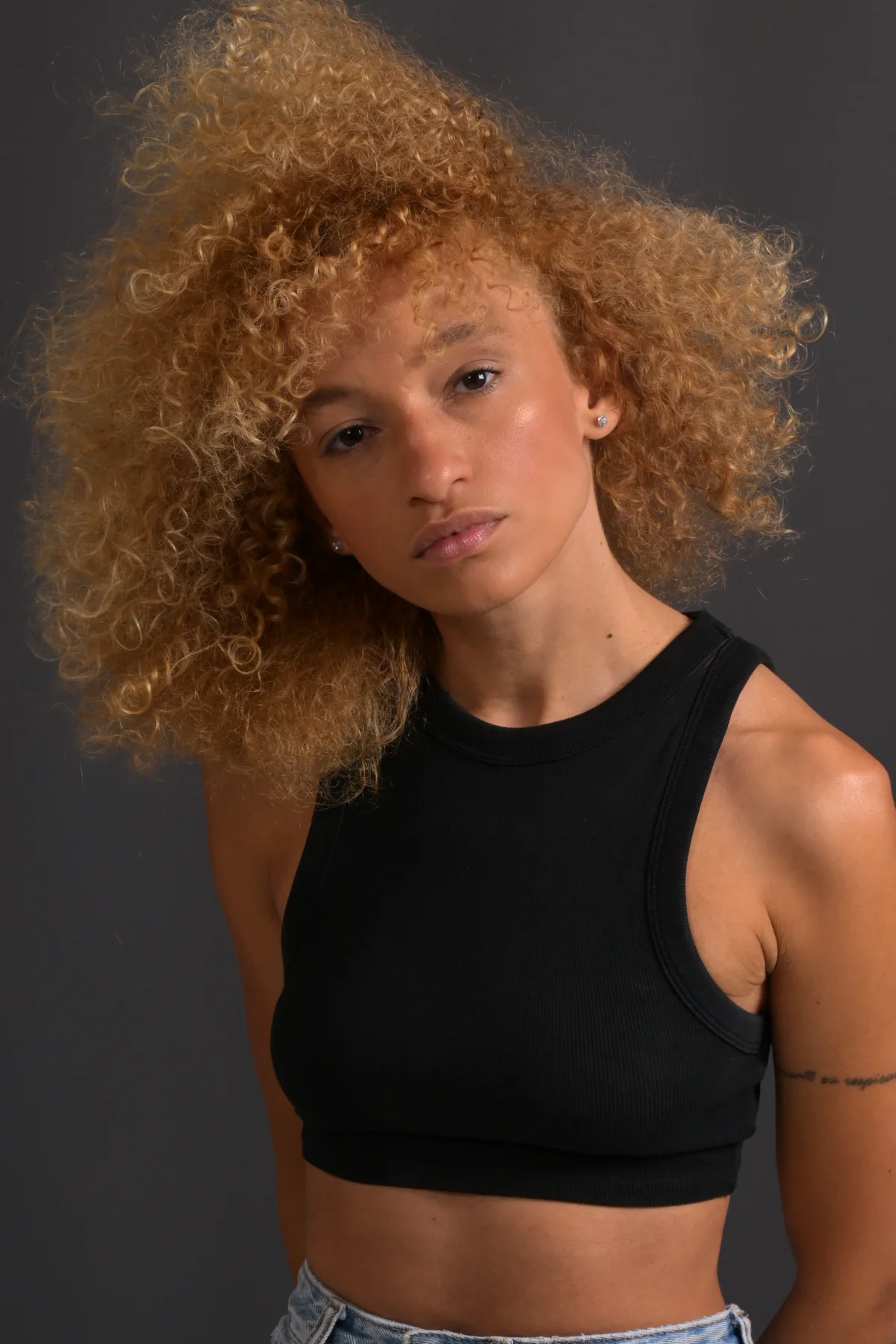 Three-quarter portrait of Nalu in a black top and jeans against a dark background.