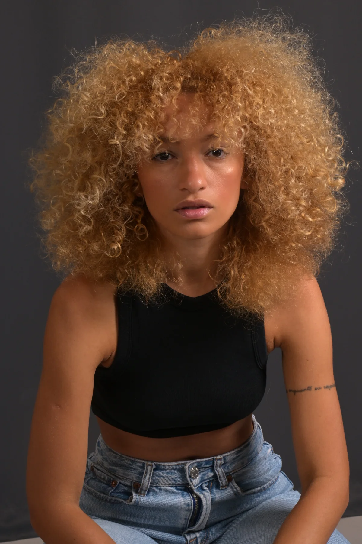Front portrait of Nalu in a black top and jeans against a dark background.
